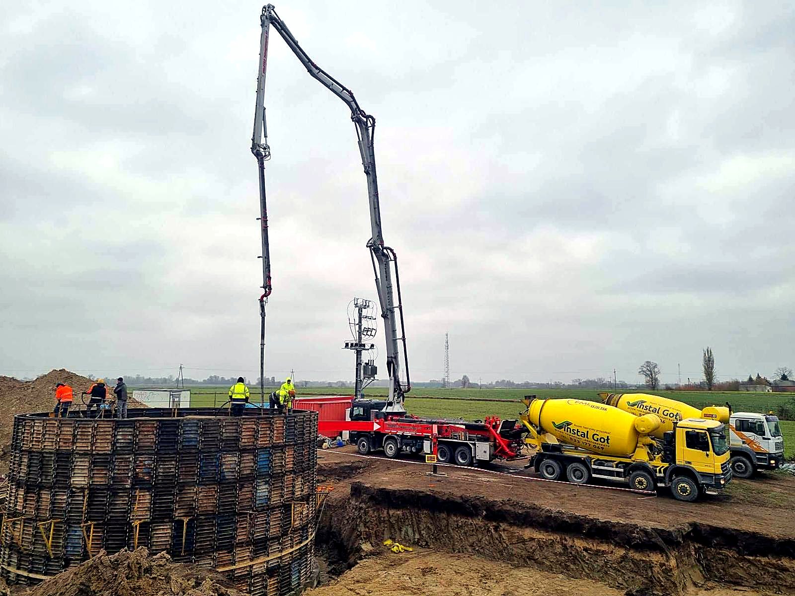 Pompa i dwie betonomieszarki przy betonowaniu okrągłego zbiornika w deskowaniu