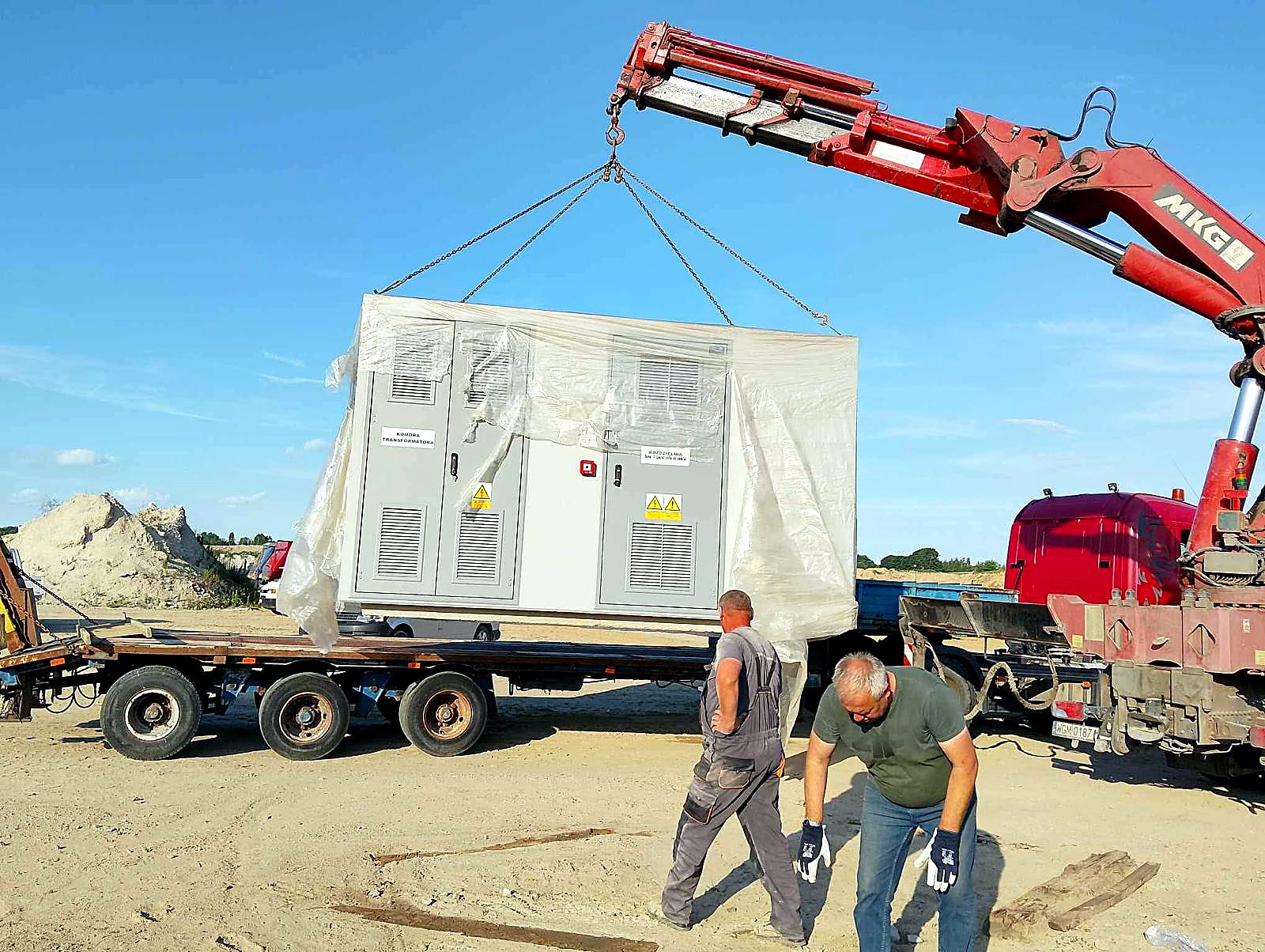 Żuraw HDS unosi prefabrykowaną stację kontenerową z naczepy