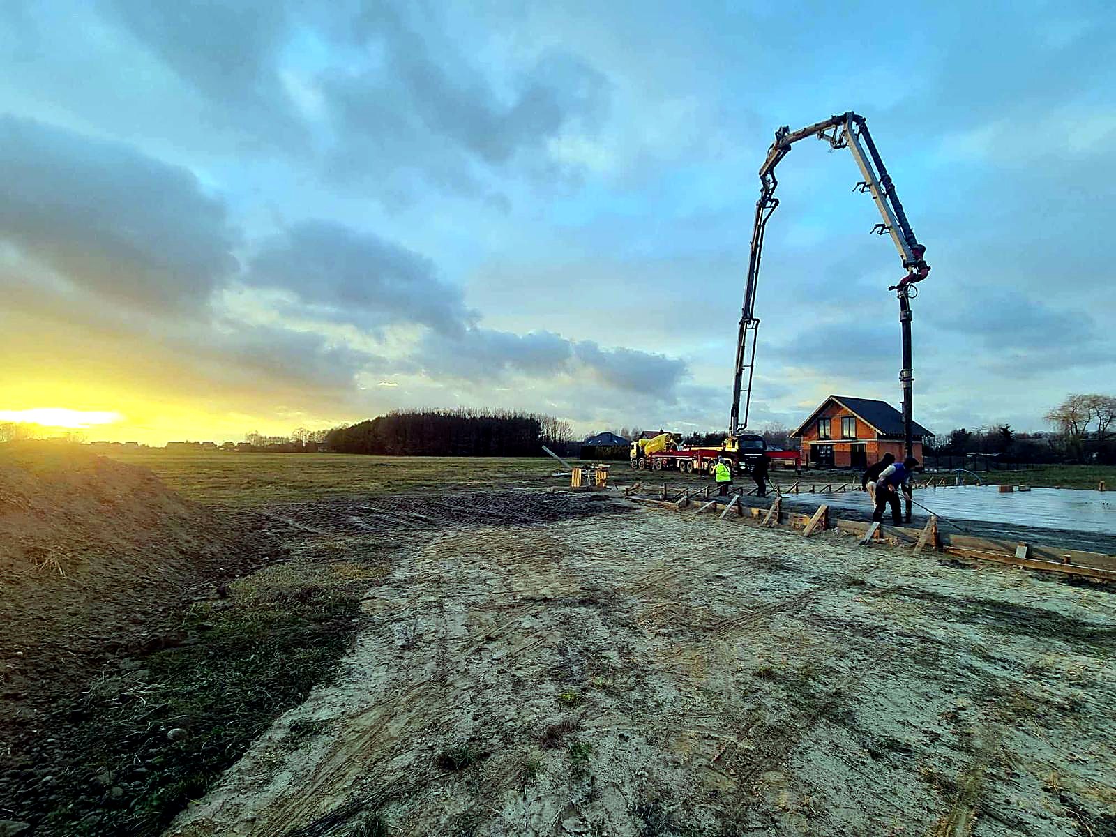 Pompa do betonu i świeżo wylana płyta przy domu jednorodzinnym o zachodzie słońca